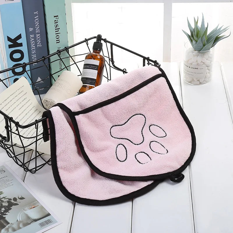 Pink towel with paw print design on a white surface with books and a plant in the background