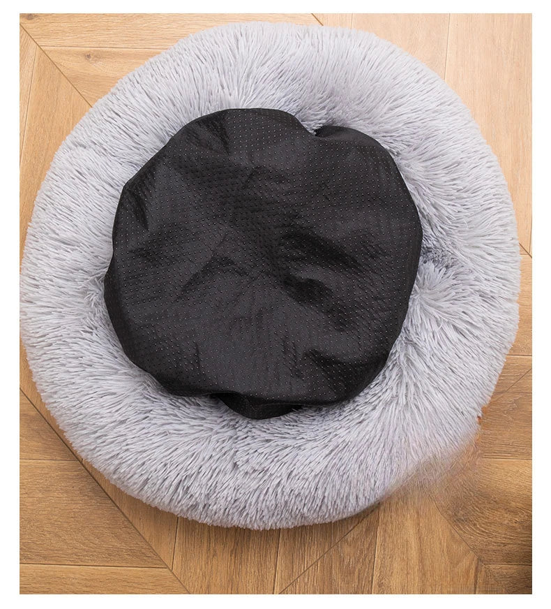 Black cushion on a fluffy gray pet bed on a wooden floor
