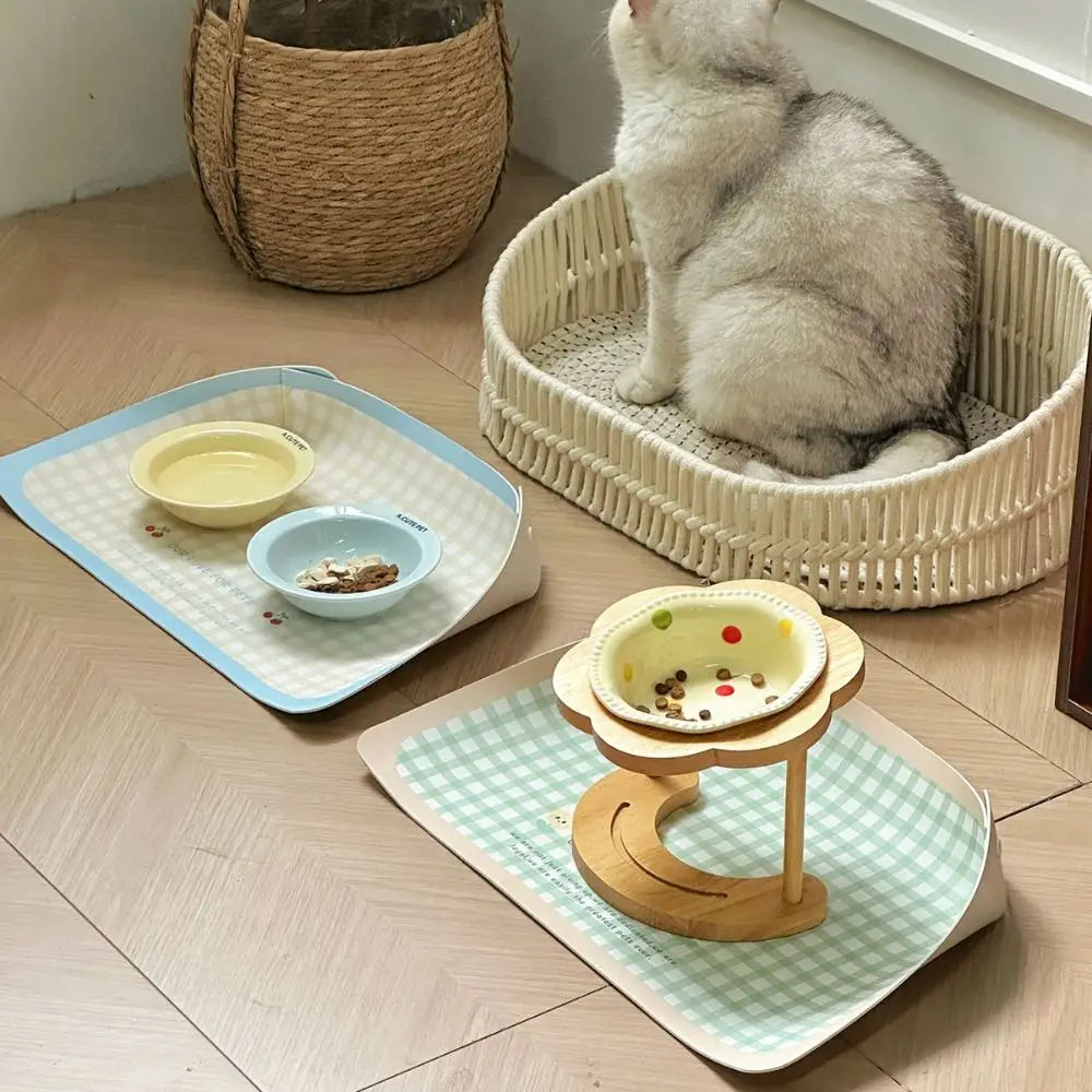 Cat sitting on a woven basket with pet bowls and a stand on checkered mats.
