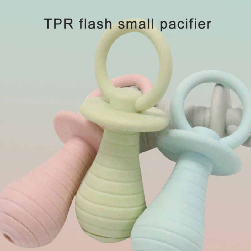 Two silicone pacifiers, one green and one light blue, held by a hand against a light background.