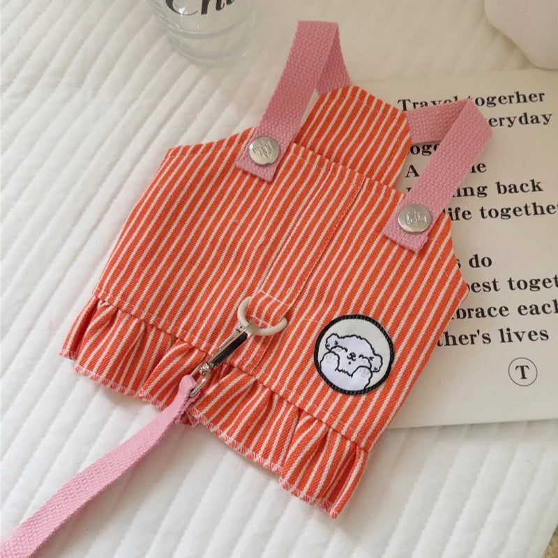Orange and white striped dog romper with pink straps on a textured surface