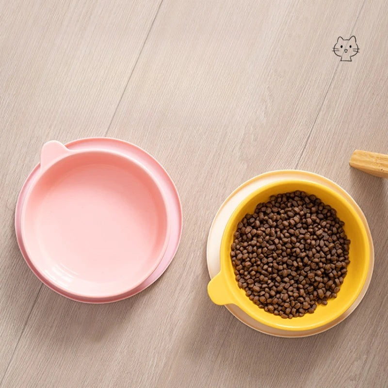 Pink and yellow pet bowls with dry cat food on a wooden surface