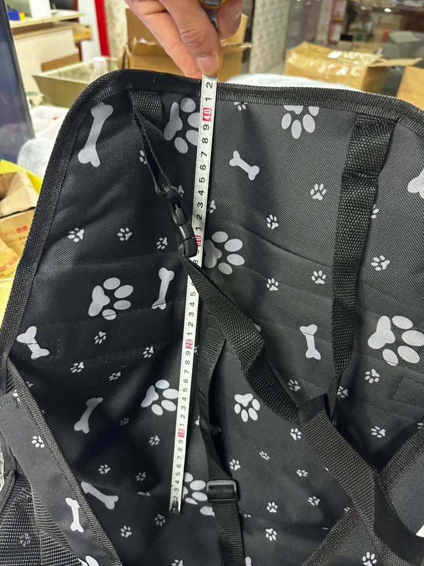 Black pet carrier with bone and paw pattern, being measured with a tape measure.