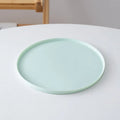 Light green ceramic plate on a white surface with a wooden chair in the background