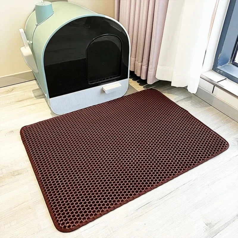 Brown mat with honeycomb pattern in front of a cat litter box on a light wood floor.