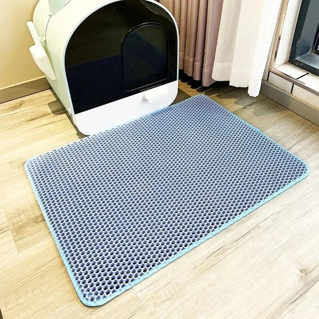 Blue mat with textured surface in front of a cat litter box on a wooden floor.