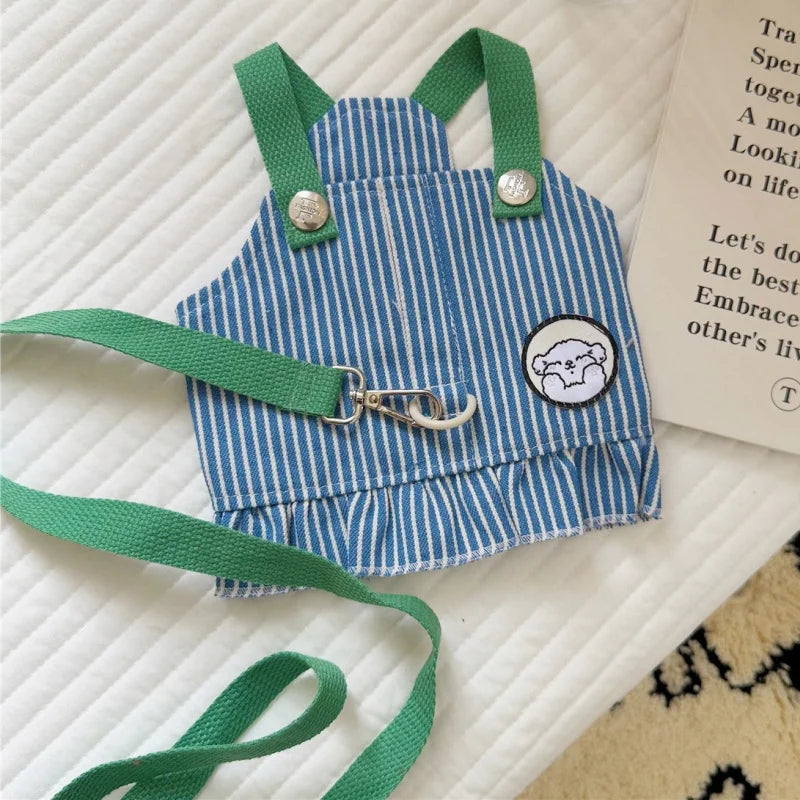Blue and white striped dog romper with green straps on a textured surface