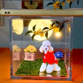Clear decorative box with a poodle figurine in a red dress, grass, flowers, and a moonlit sky background.