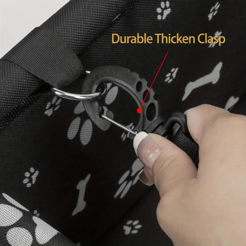 Hand using a tool to demonstrate the durability of a thickened clasp on a black bag with paw print patterns.
