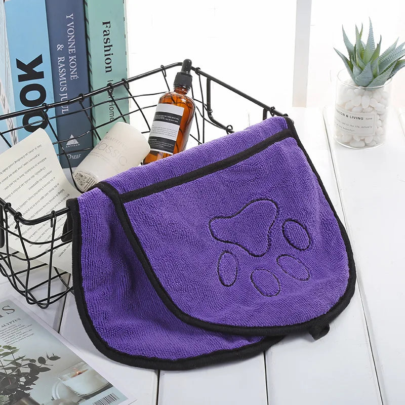 Purple towel with paw print design on a table with books and a plant in the background
