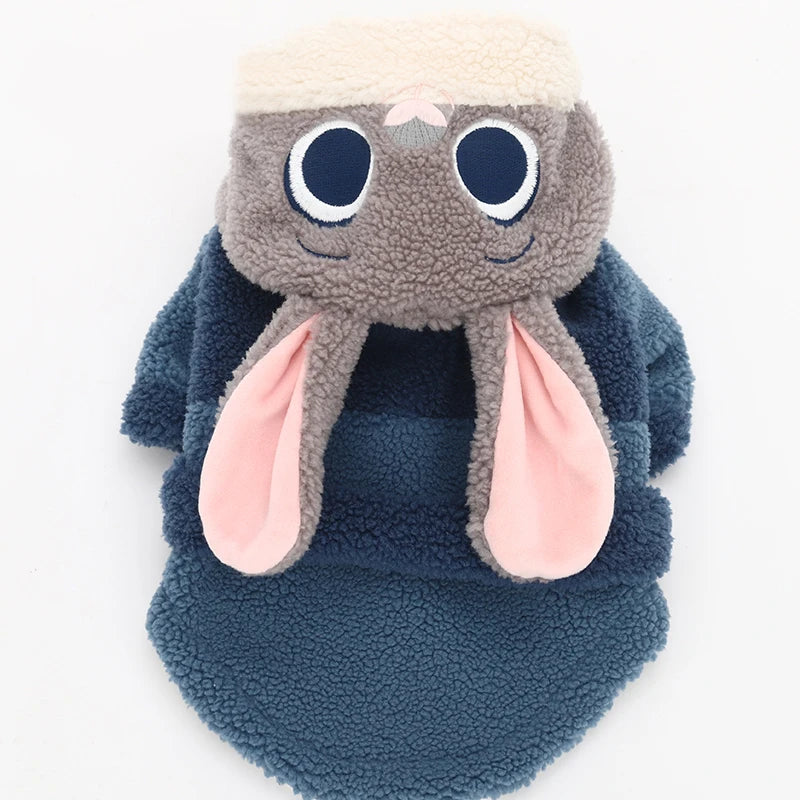 Plush toy resembling a creature with large eyes and pink ears, wearing a blue outfit on a white background.