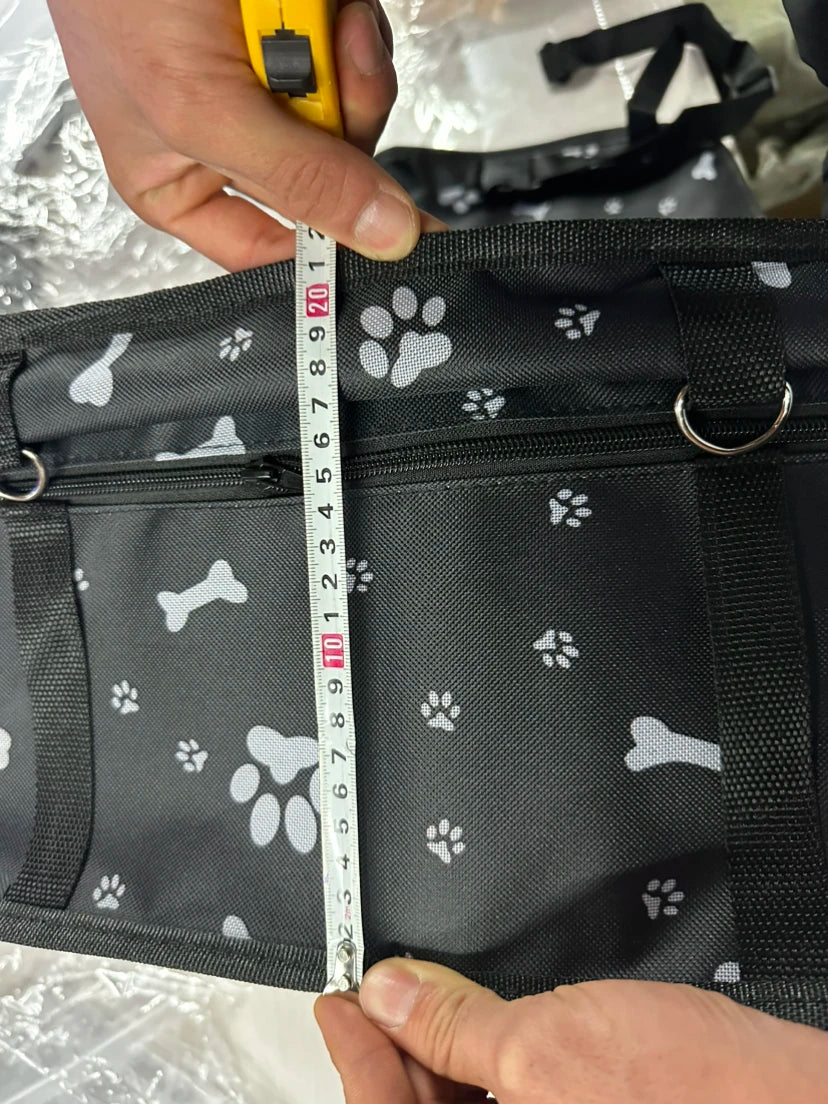 Measuring a black bag with paw print patterns using a tape measure.