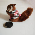 Small stuffed animal in a striped outfit with a pink bow, standing next to a black leash on a light background