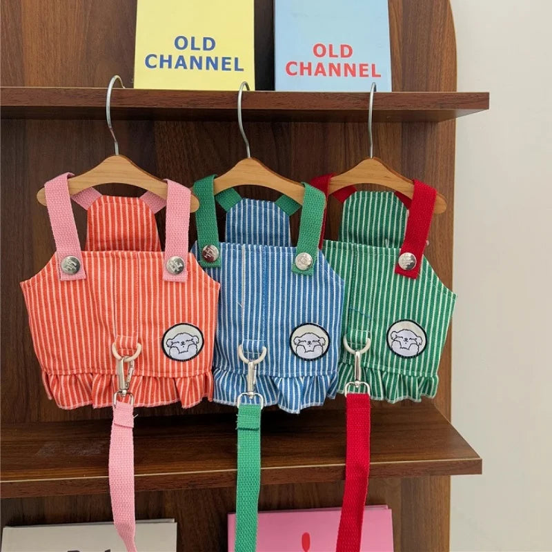 Three colorful pet overalls with straps hanging on a wooden shelf.