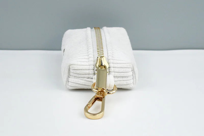 White pouch with gold zipper and clasp on a white surface with gray background