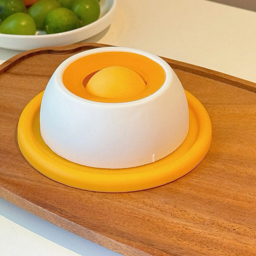 White and orange kitchen tool on a wooden surface with green fruits in the background
