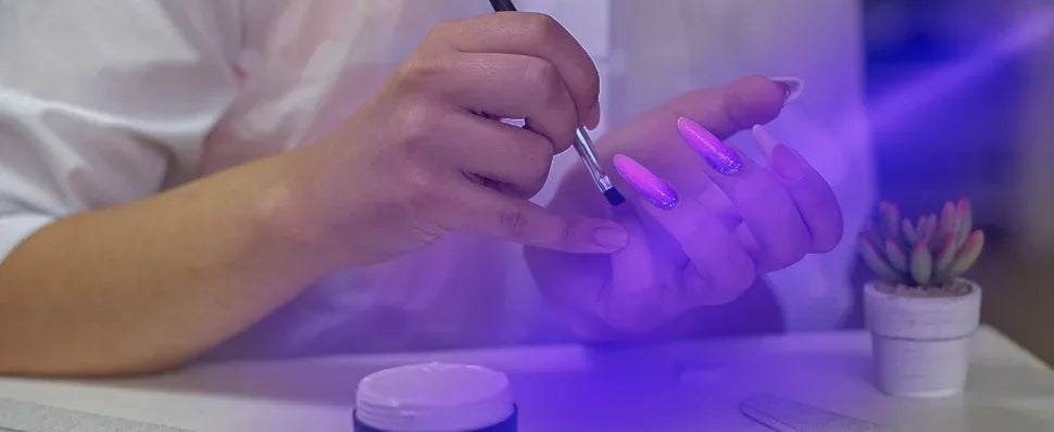 Person with neon purple nail polish painting their nails with a brush, illuminated by a purple light.