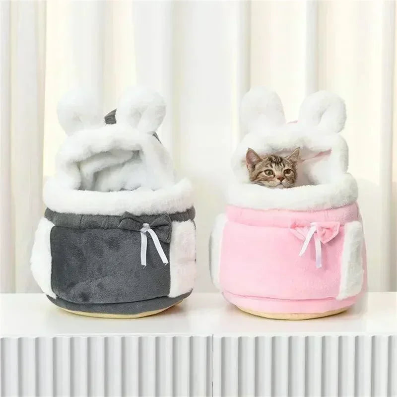 Two pet beds, one gray and one pink, with a cat peeking out from the pink bed.