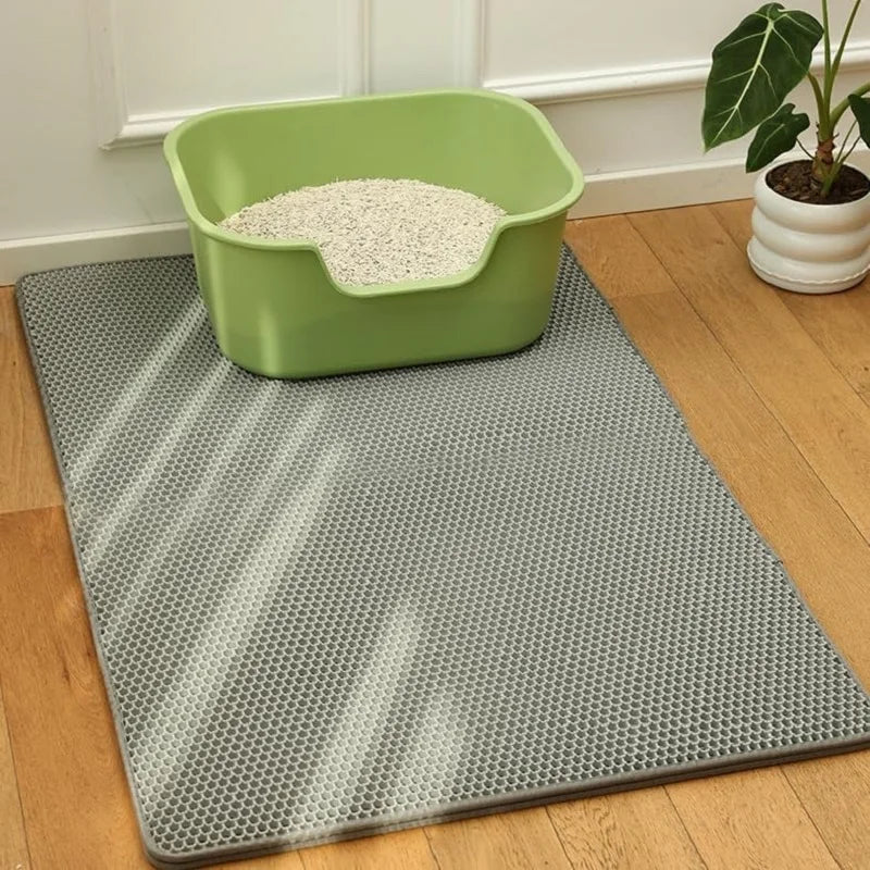 Green cat litter box on a gray mat with a plant in the background